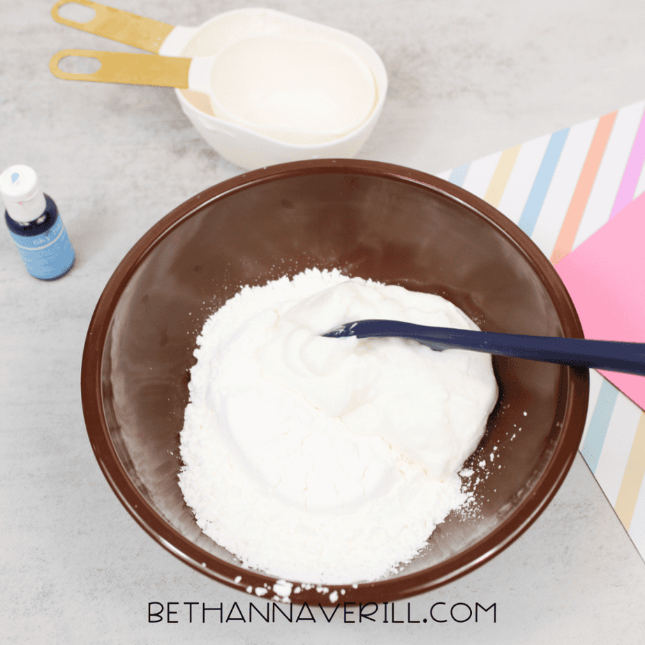 White mixture and powder in a brown mixing bowl with a blue spoon resting inside.