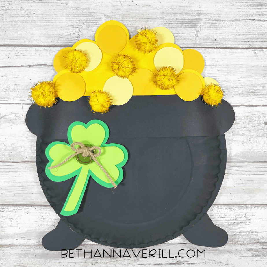 Image of the completed Paper Plate Pot of Gold craft featuring layered gold coins, yellow pom poms, and a green shamrock on the front.
