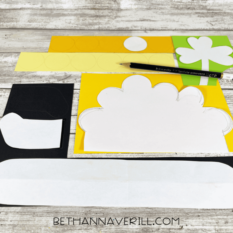 Image showing cardstock pieces traced with pot, shamrock, and gold coin patterns along with cut yellow paper circles and black pot shapes.