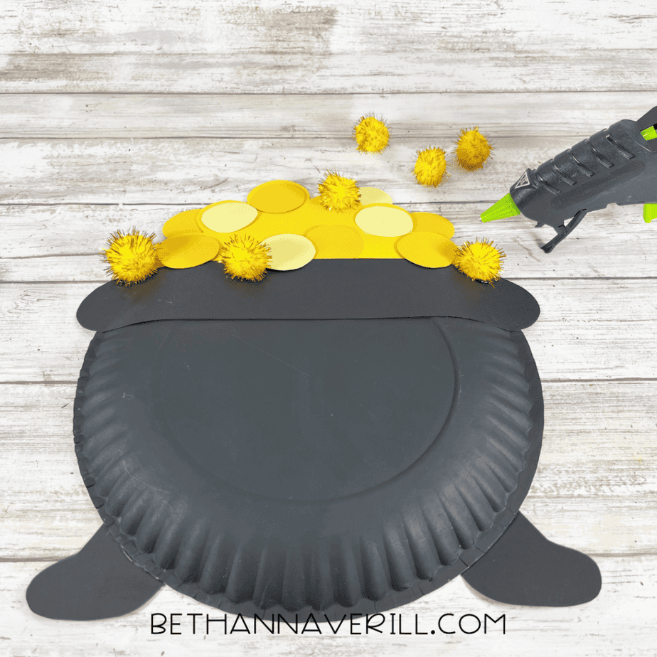 Image showing yellow pom poms being glued on top of the paper gold coins for texture.