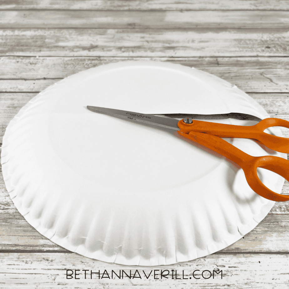 White paper plate with orange scissors placed across the center on a wood surface.