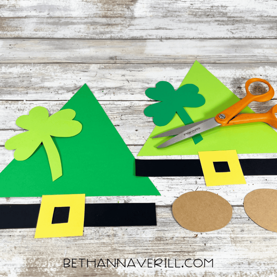 Paper plate piece with green cardstock triangle hat, black hat band, yellow buckle, and brown circle attached.