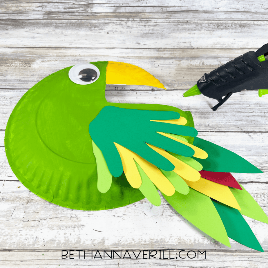 Layered cardstock feather shapes attached to the green painted paper plate.