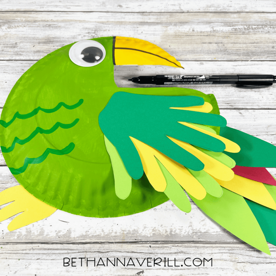 Black marker being used to add finishing touches to the parrot paper plate craft.