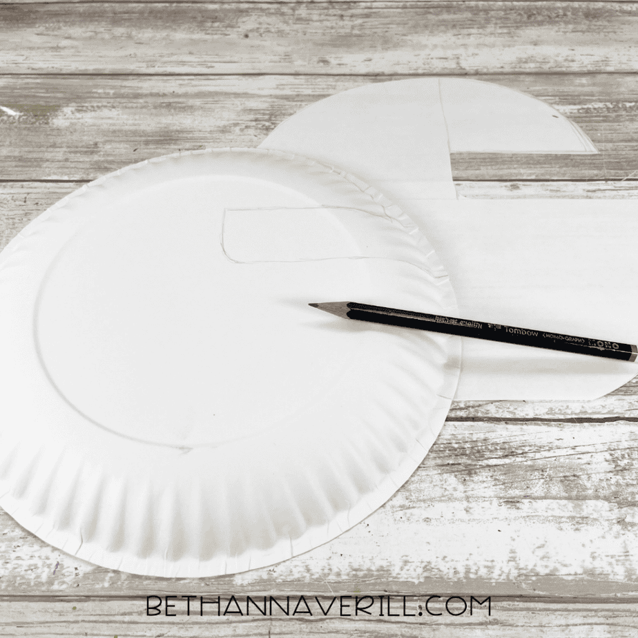 Paper plate with a curved shape drawn on it using a pencil, with a paper pattern piece nearby.