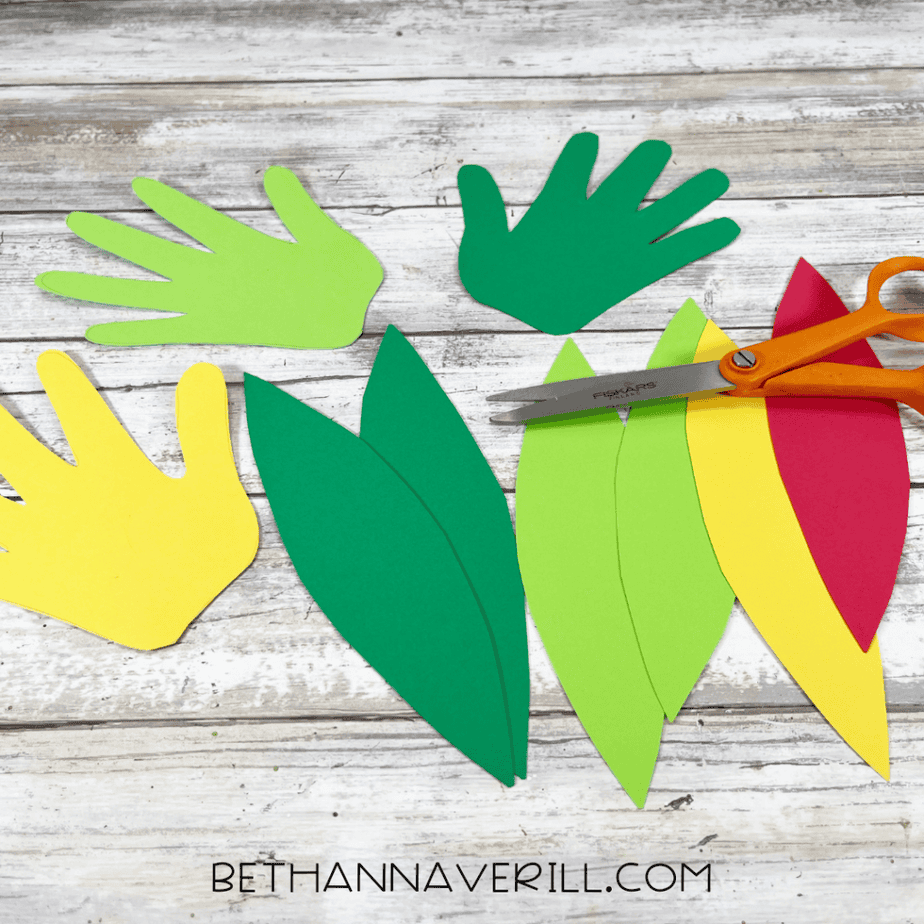 Cut out cardstock shapes including hand shapes and long curved feather shapes in green, yellow, and red.