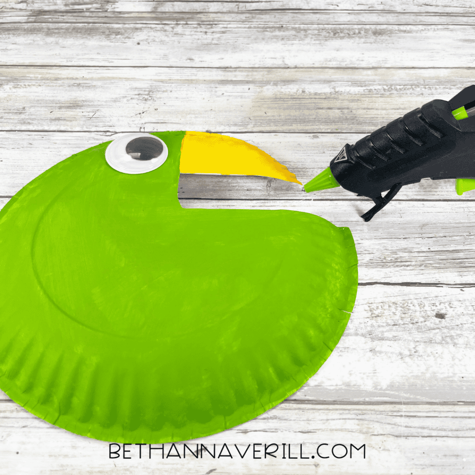 Green painted paper plate with a googly eye attached and a hot glue gun nearby.
