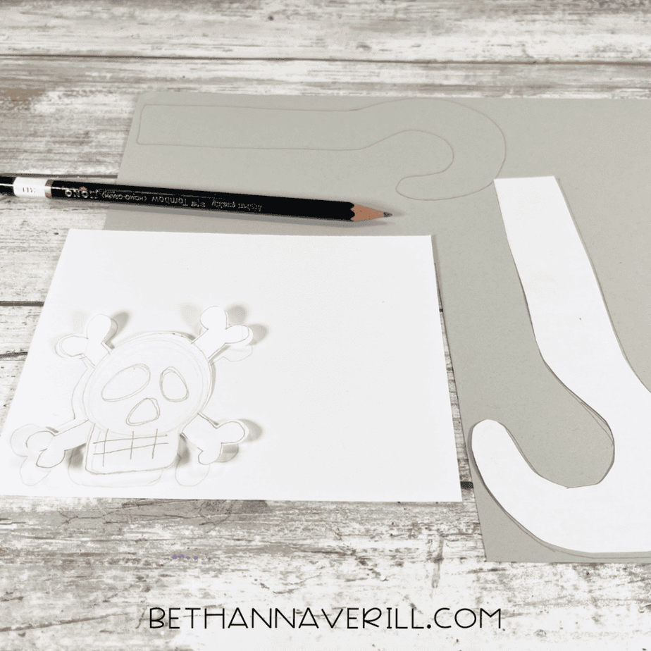 Printed skull and hook patterns on paper with a pencil and gray cardstock.