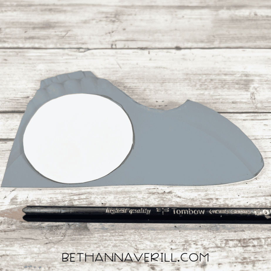 Gray painted paper plate cut into an anchor shape with a small circular piece and scissors nearby.