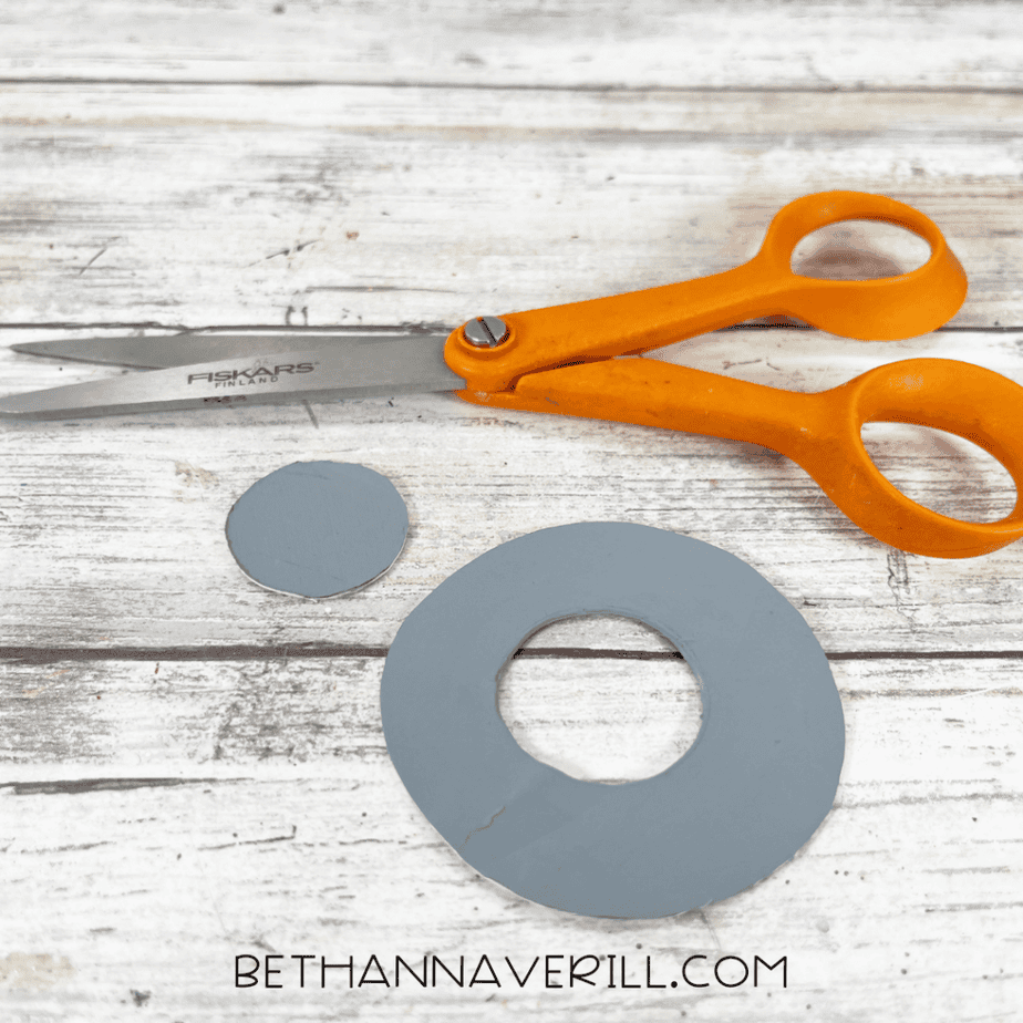 Small gray circular paper plate piece being glued to the top of a gray anchor shape with a hot glue gun.