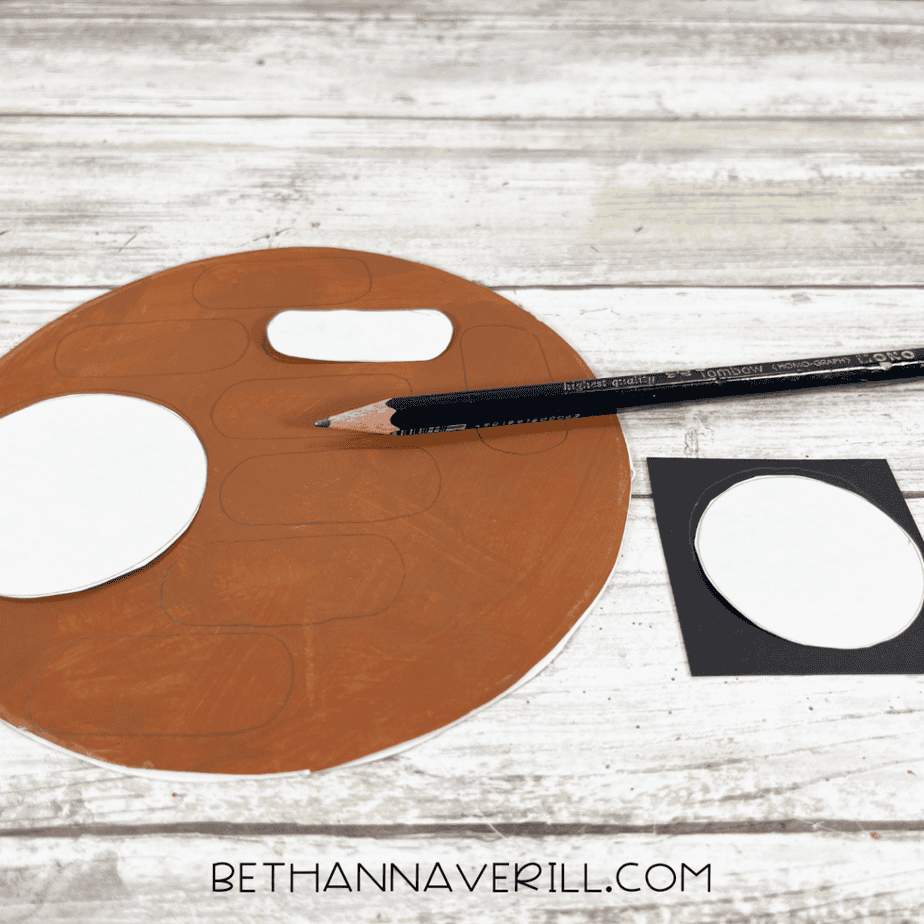 Brown-painted paper plate with oval shapes traced on the surface and paper templates nearby with a pencil.