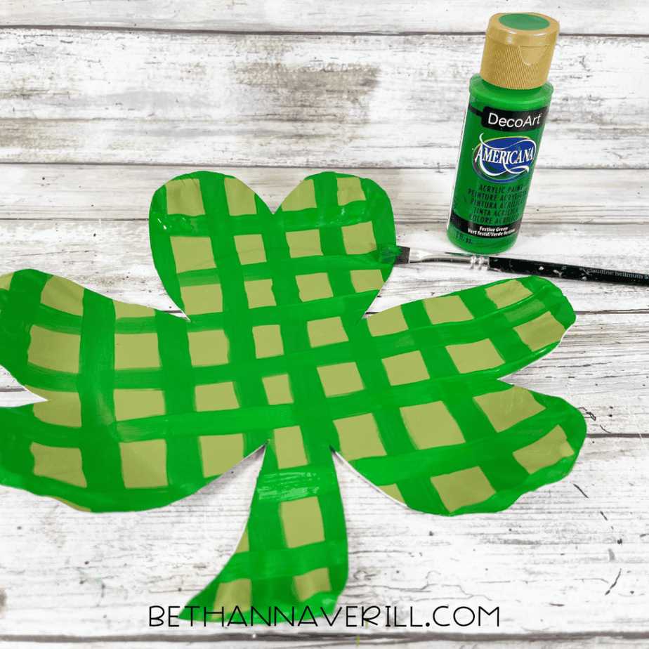 Shamrock cutout painted with a green grid pattern and a paintbrush resting nearby.