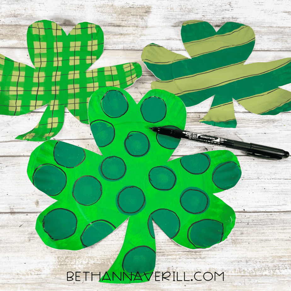Three finished shamrock cutouts with different painted patterns and a black marker outlining details.