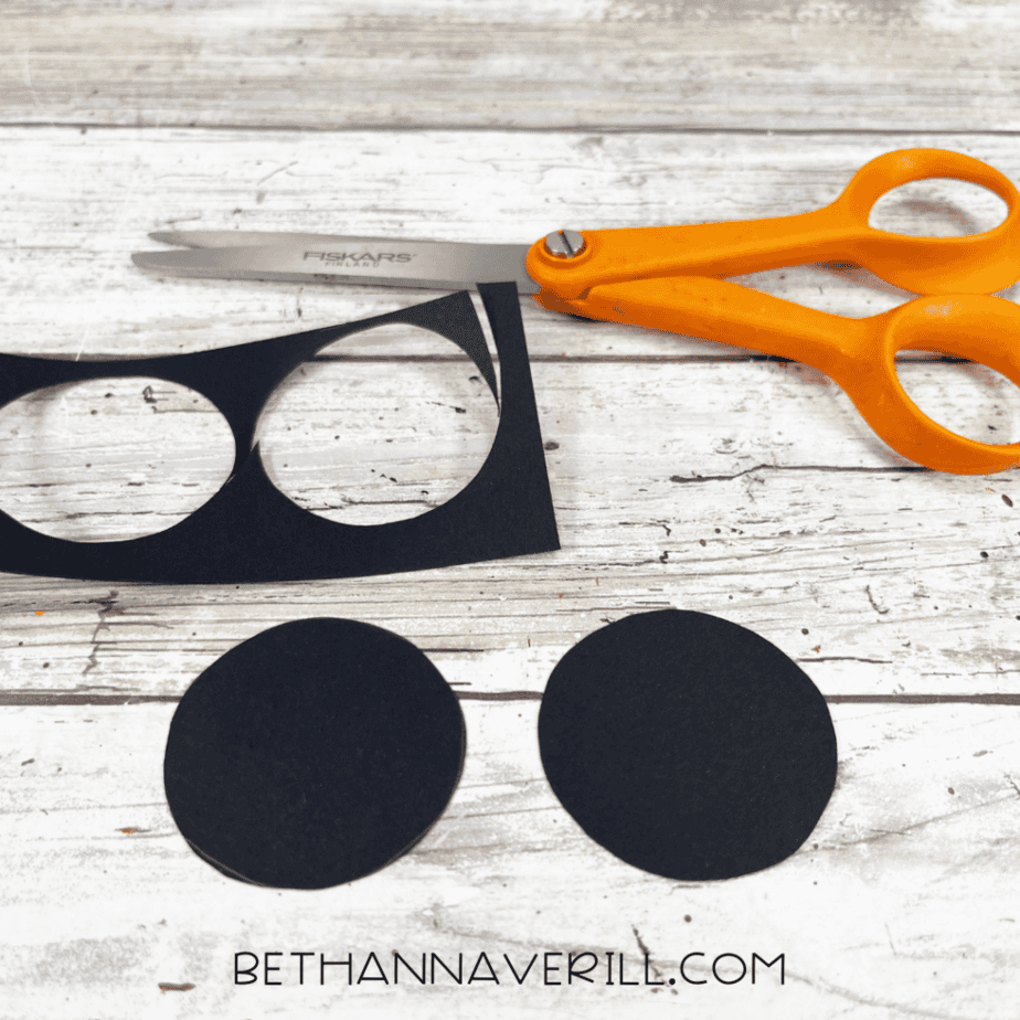 Black cardstock circles cut out with scissors to make wheels for a popsicle stick craft project.