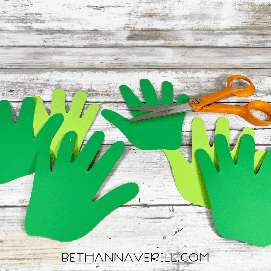 Several hand-shaped pieces cut from green and light green paper with scissors placed on top.