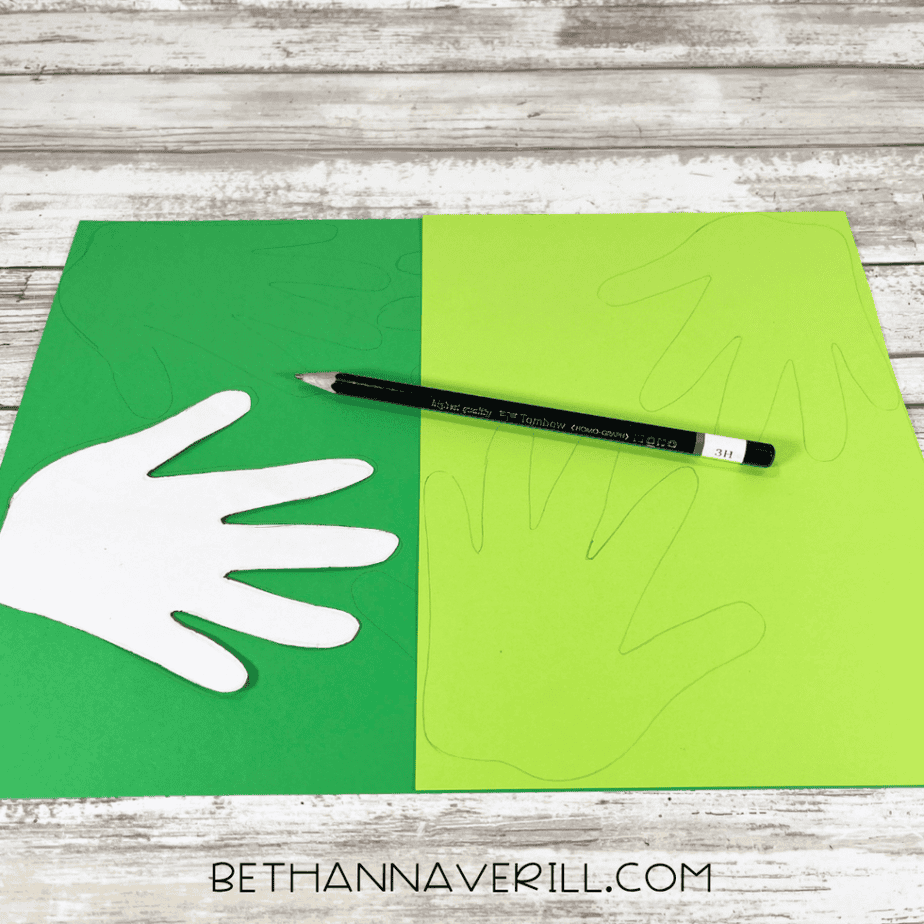 Green and light green paper sheets with hand shapes traced on them using a pencil and a white hand-shaped template nearby.