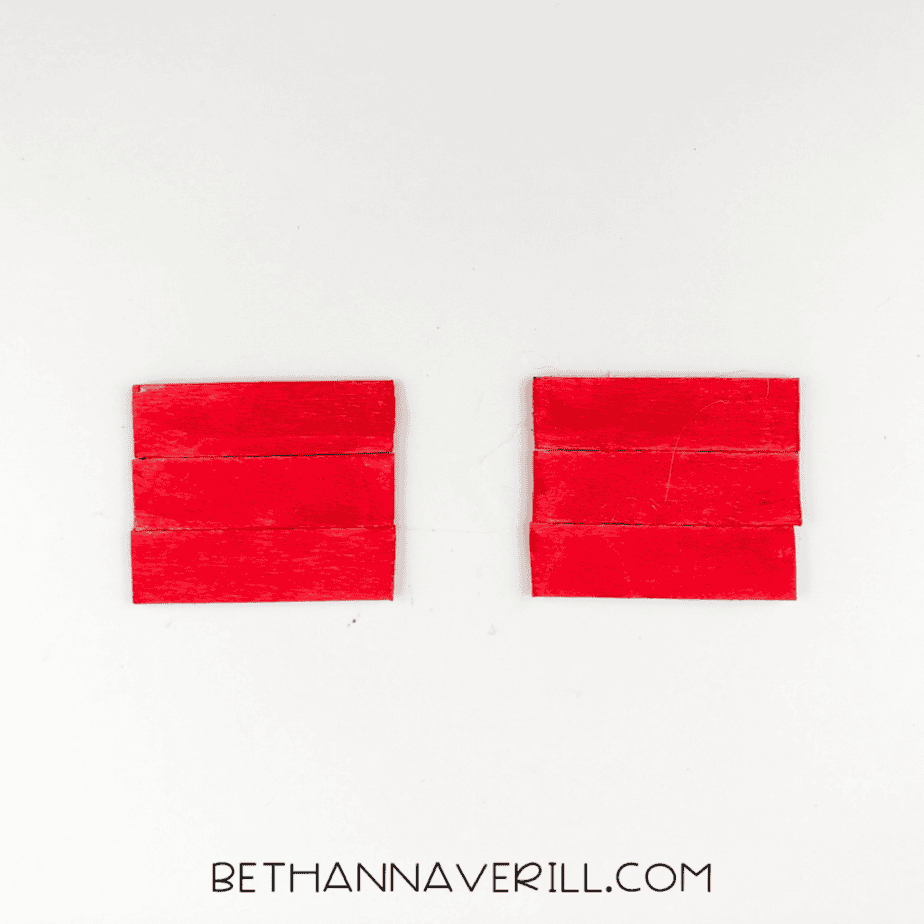 Six red-painted craft sticks arranged into two groups of three on a white background.