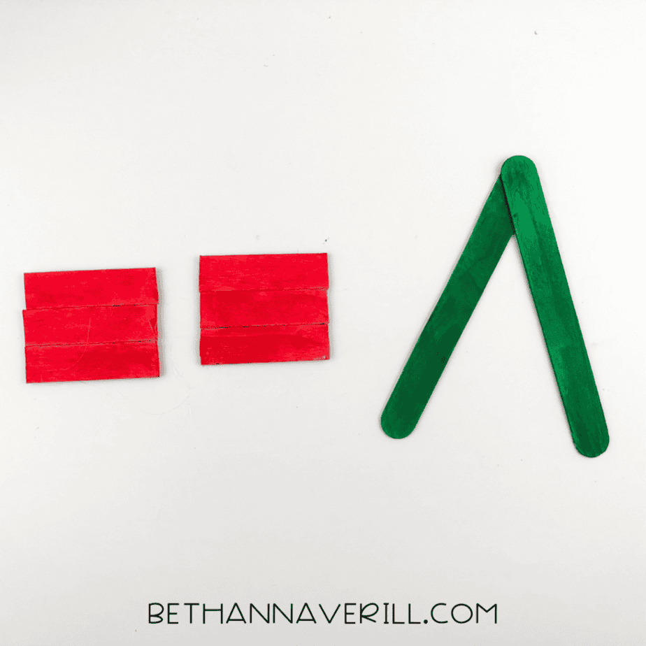 Two groups of three red-painted craft sticks on the left and two green-painted craft sticks arranged in an inverted V shape on the right.