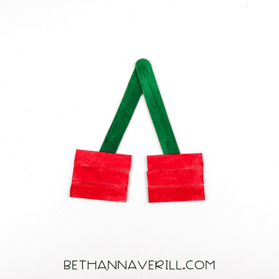 Two sets of three red-painted craft sticks with two green-painted sticks attached above them forming a connected shape.