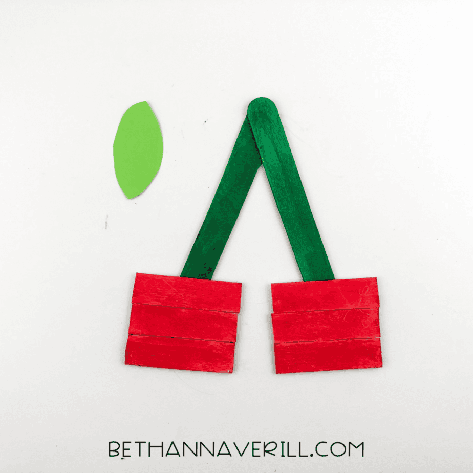 The same arrangement with a small green paper leaf shape placed to the left of the green sticks.
