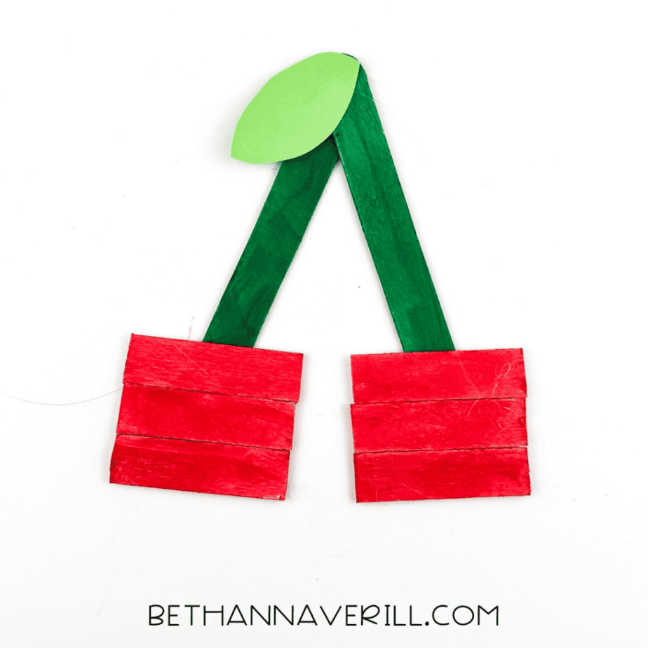 The green paper leaf attached to the top of the green sticks above the red craft stick groups.