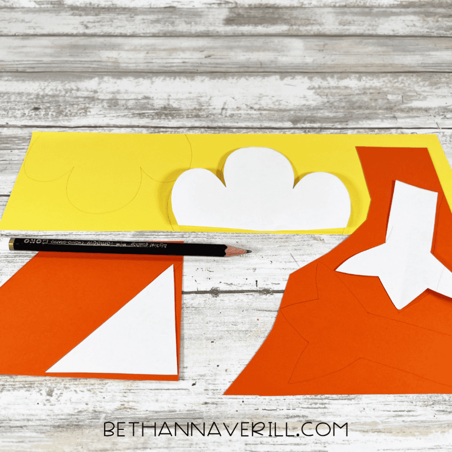 Yellow and orange paper with shapes traced and cut out, including wing shapes and a triangular piece for a beak.