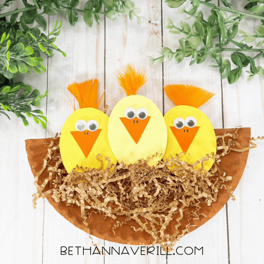 The finished arrangement shows three yellow oval shapes with googly eyes and orange pieces, sitting on shredded brown paper attached to the plate half. Green decorative plants appear at the top edge of the frame.