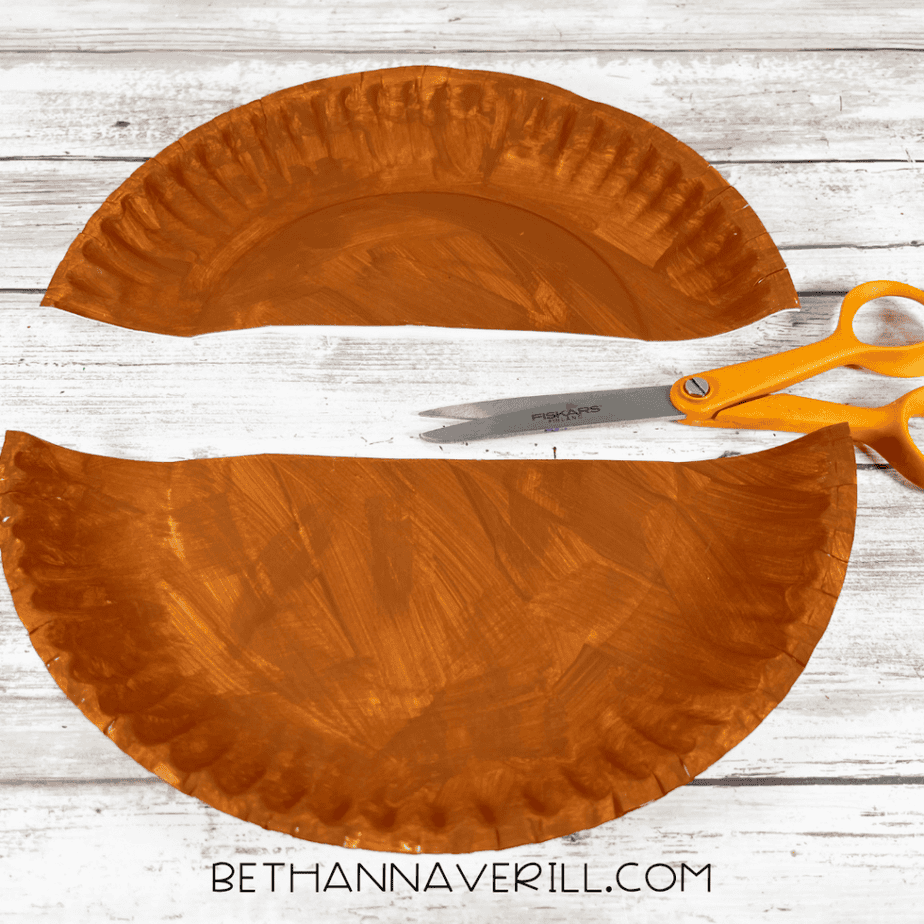 The painted plate has been cut into two curved halves. A pair of scissors lies next to them.