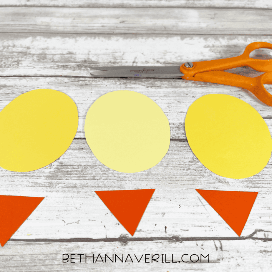 Three yellow oval cutouts and three orange triangle cutouts are arranged on the surface. Scissors are nearby.