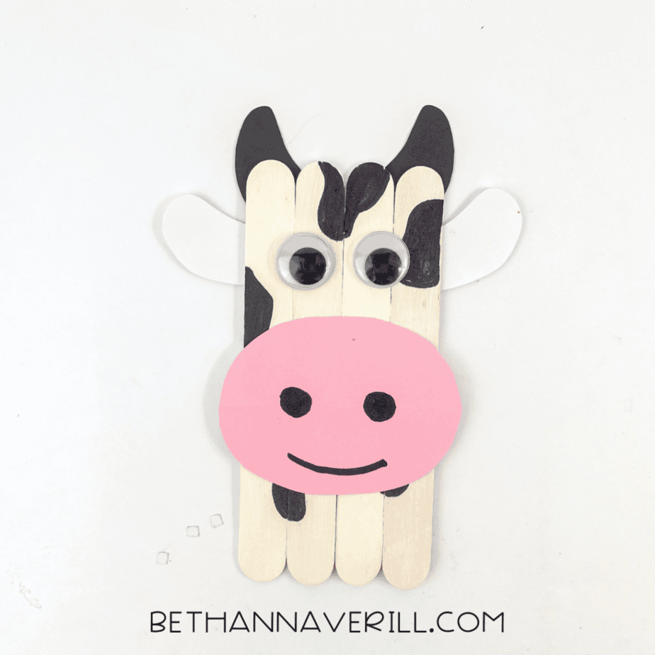 A closer view of the assembled piece shows four vertical wooden sticks with googly eyes, a pink oval shape, black markings, black shapes at the top, and white shapes on each side.