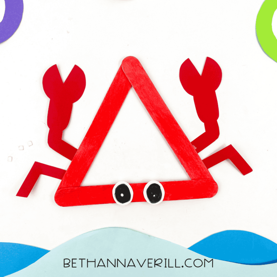 Completed red popsicle stick craft with paper claws and legs placed above blue paper shapes