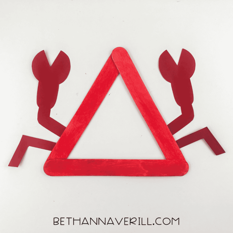 Red popsicle stick triangle with attached claws and additional leg shapes added on both sides