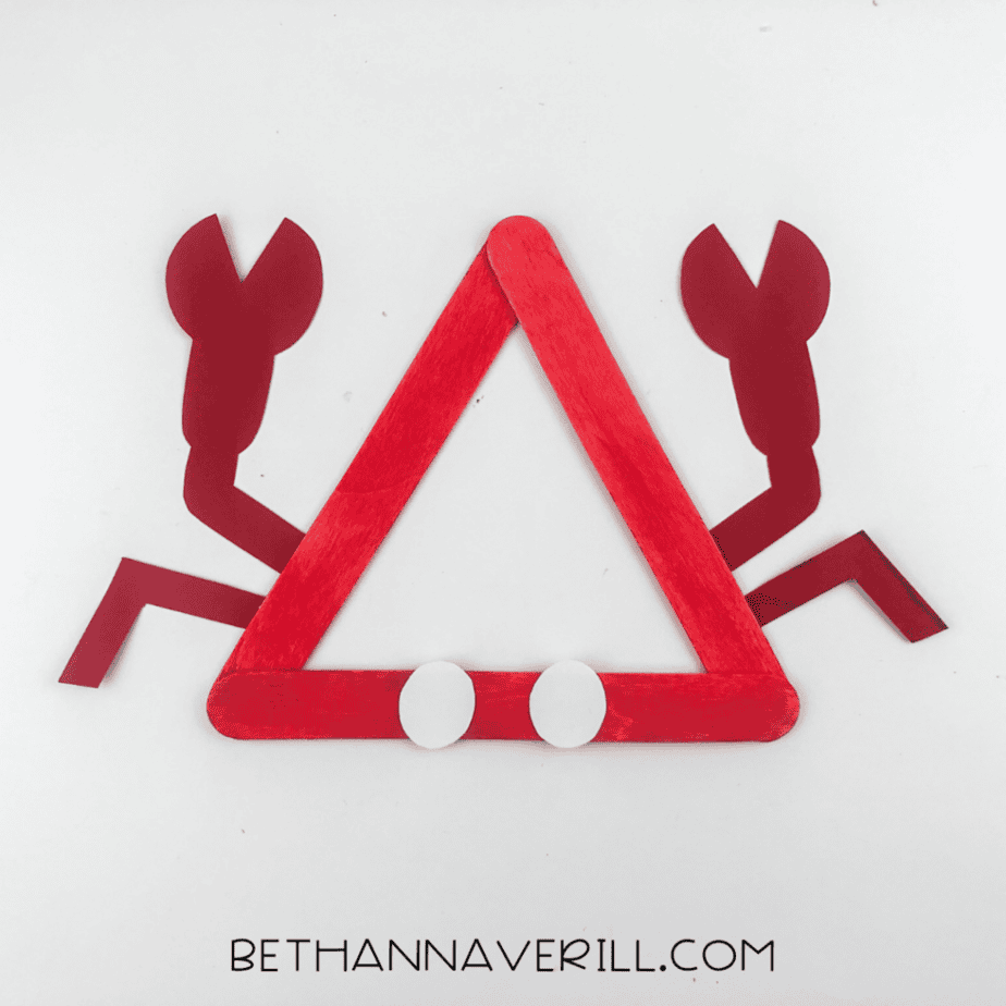 Red popsicle stick triangle with paper claws, legs, and two white circles placed at the bottom