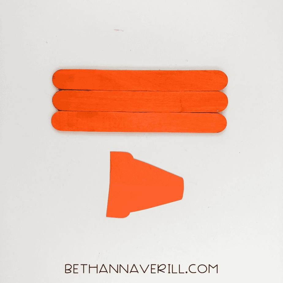 Three painted popsicle sticks aligned horizontally with a cut orange paper piece below