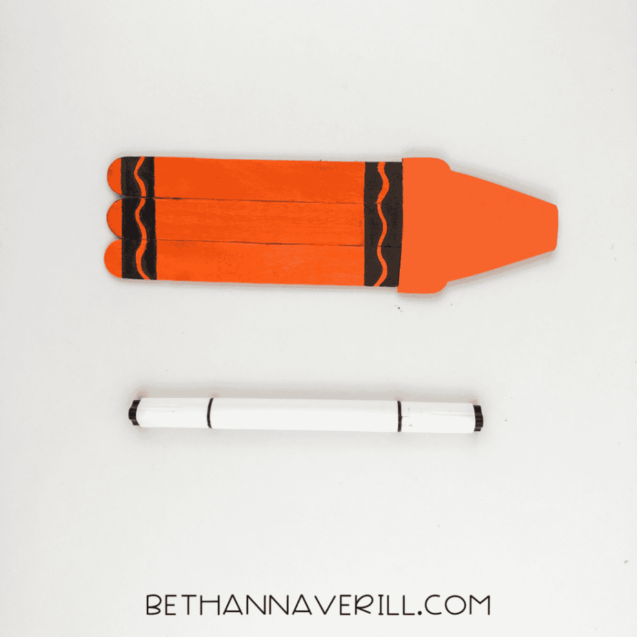 Orange popsicle stick craft with black decorative lines drawn across the sticks and a marker below