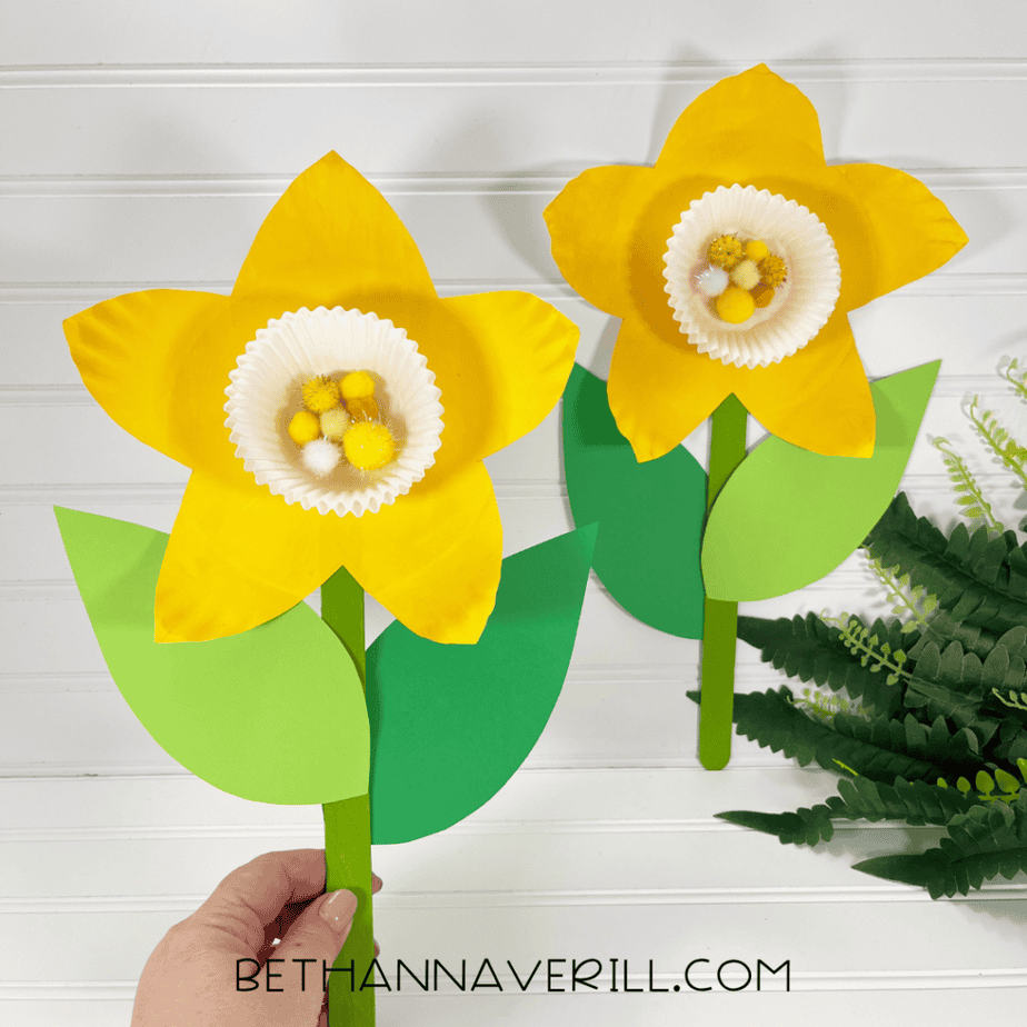 Finished paper plate daffodil craft with green leaves and pom pom center displayed upright.