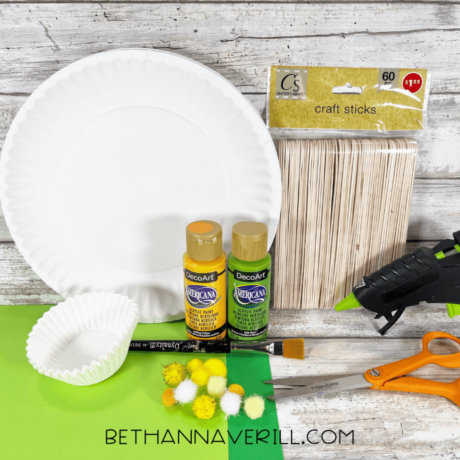 Craft supplies including paper plates, acrylic paint, craft sticks, glue gun, scissors, pom poms, and paper.