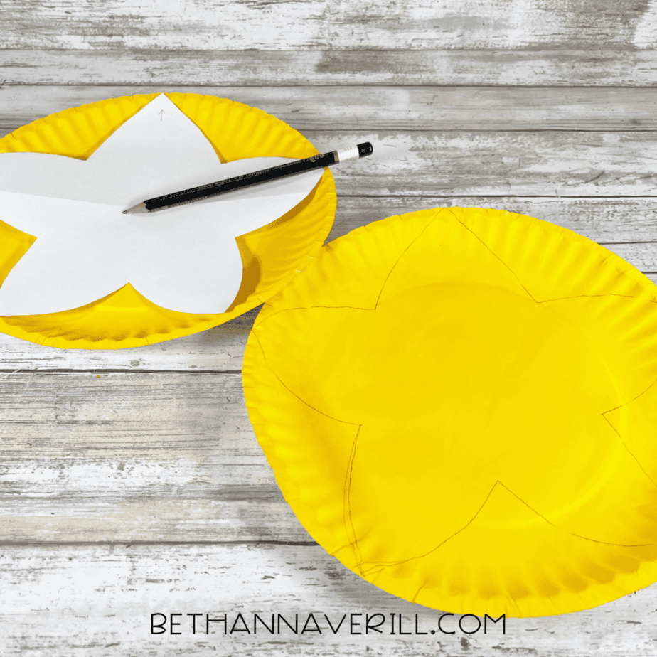 Yellow paper plates with a flower shape traced on one and a paper template with pencil.