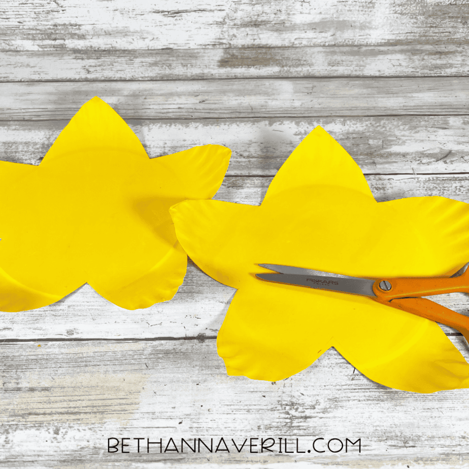 Scissors cutting along the traced flower shape on painted paper plates.