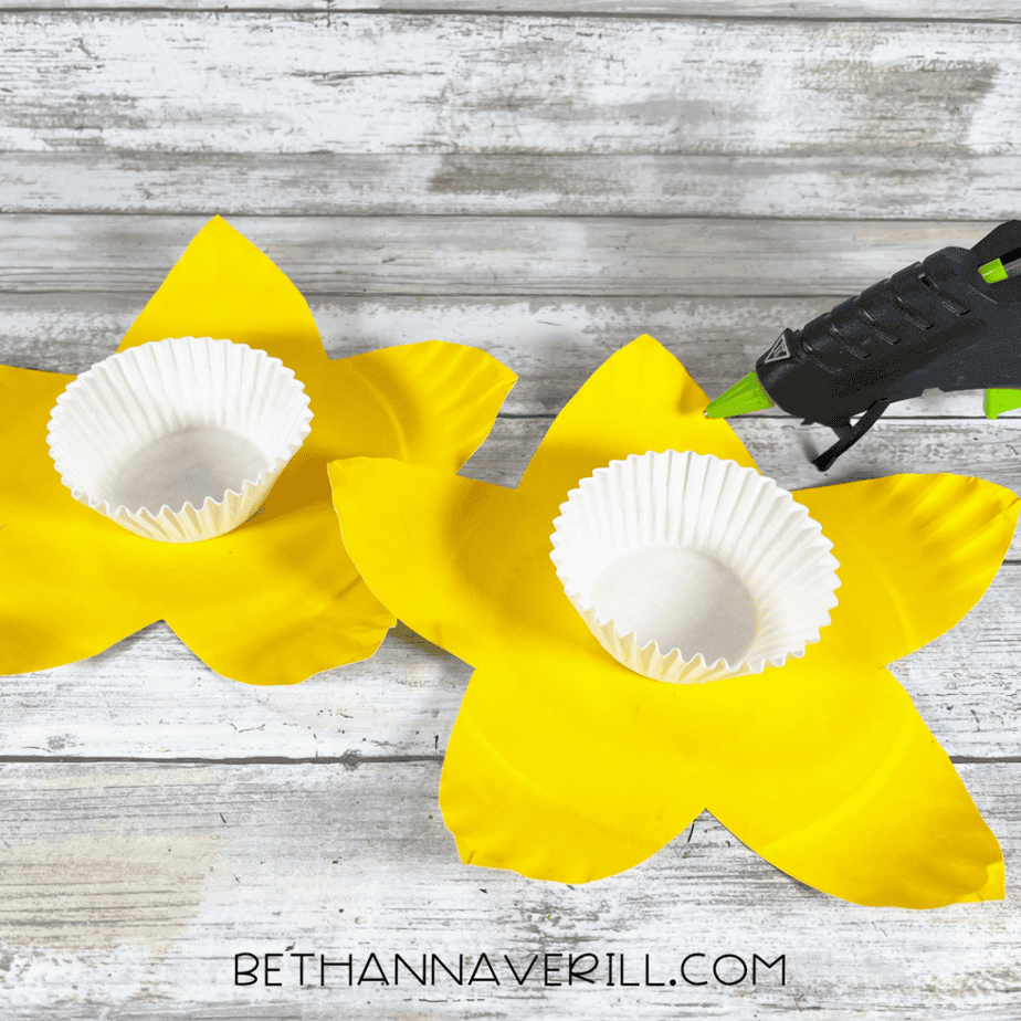 Paper cupcake liners placed in the center of yellow flower-shaped plates with glue gun nearby.