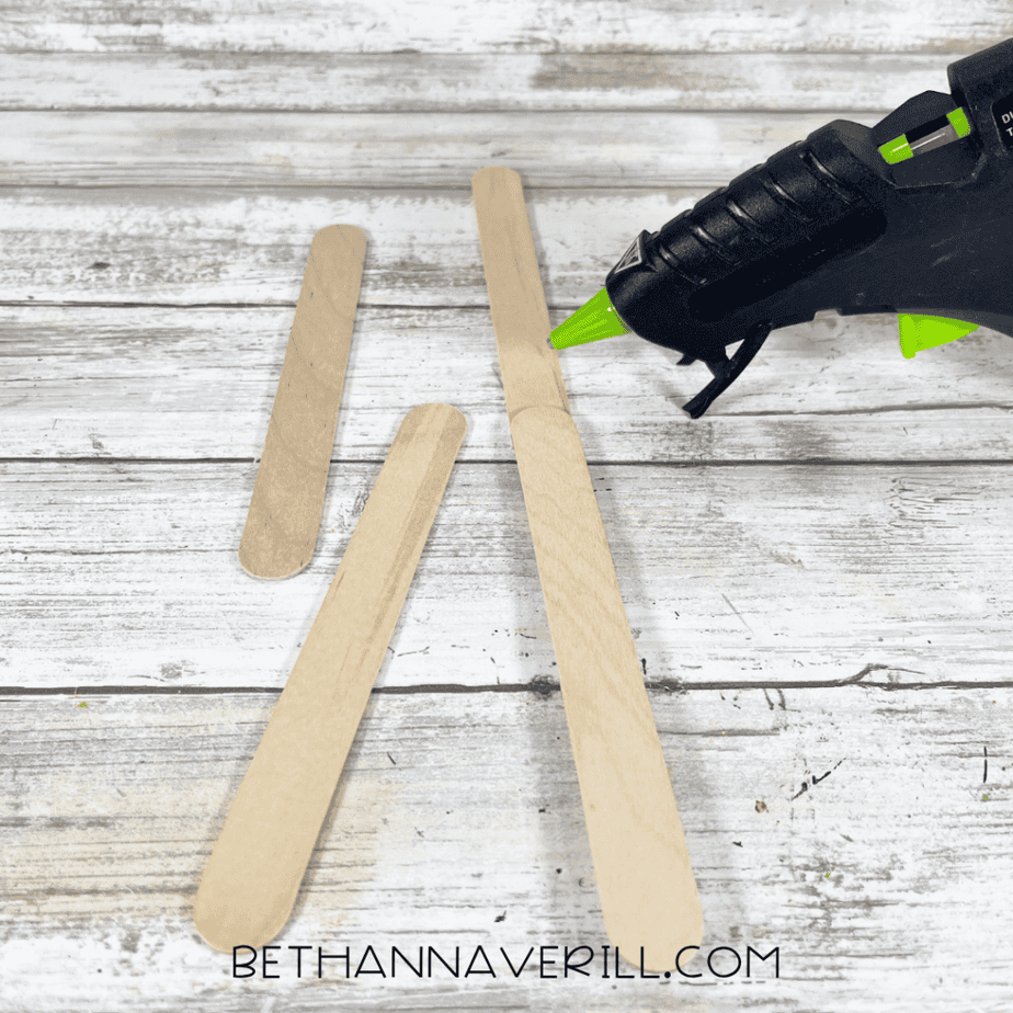 Wooden craft sticks being glued together with a hot glue gun.