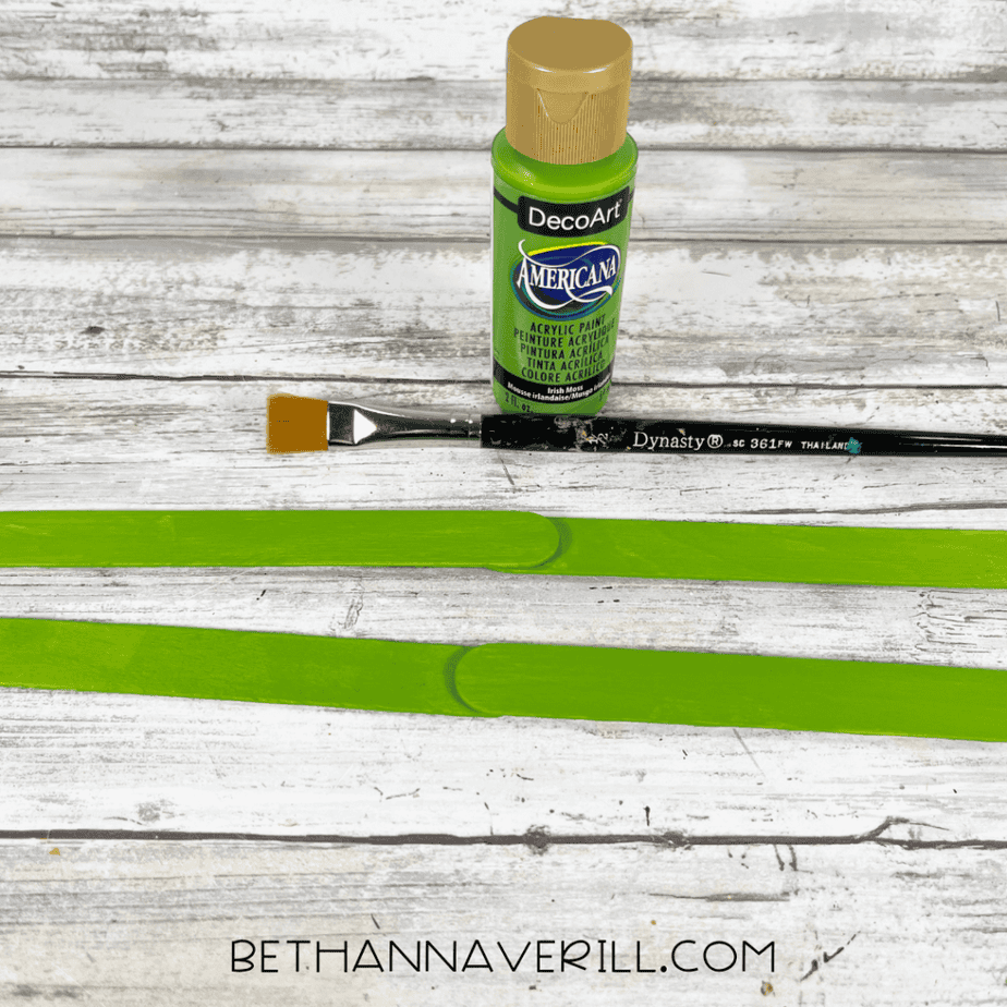 Green-painted craft sticks with paint bottle and brush above.
