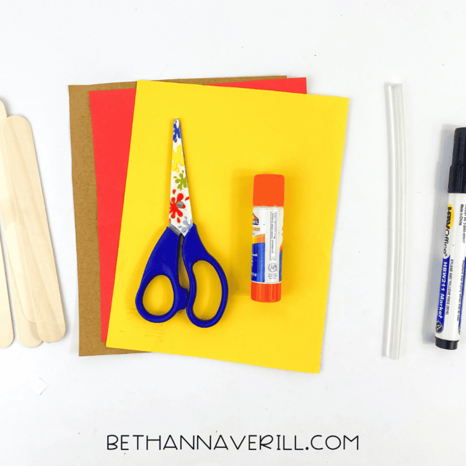 Craft supplies for a dog popsicle stick craft including wooden craft sticks, colored cardstock, scissors, glue stick, hot glue stick, and marker on a white background.