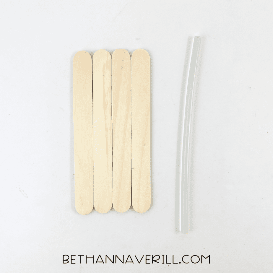Four wooden craft sticks arranged side by side next to a clear hot glue stick for a popsicle stick dog craft.