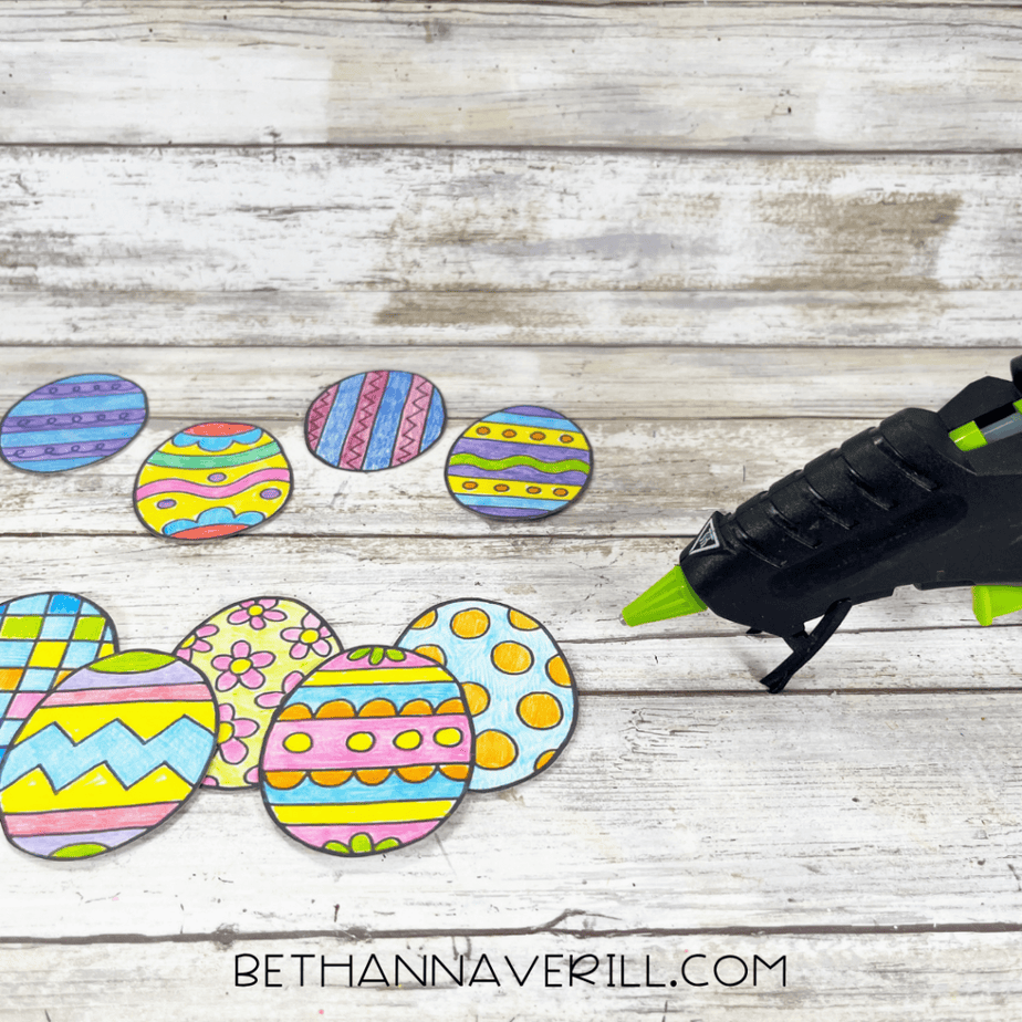 Colored paper Easter eggs and a hot glue gun on a wood background