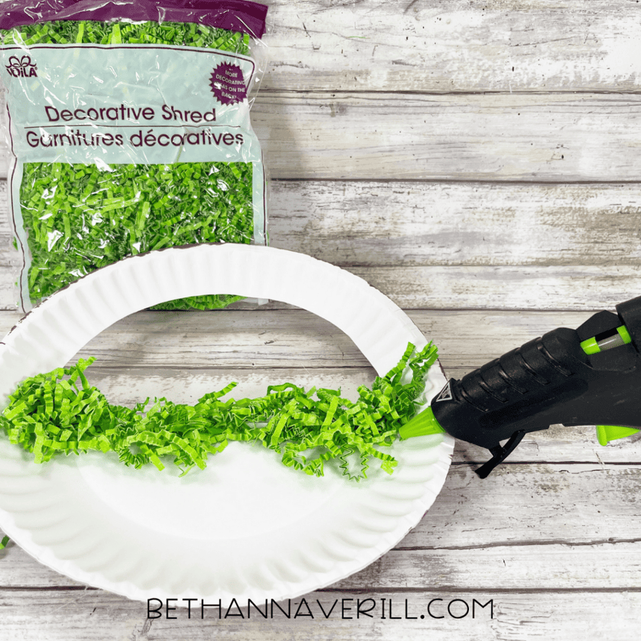 Decorative green paper shred being glued onto a paper plate basket