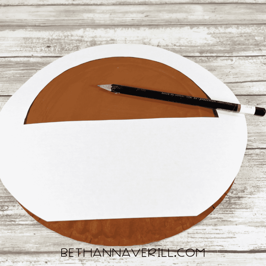 Paper template placed over a painted paper plate with pencil for tracing basket shape