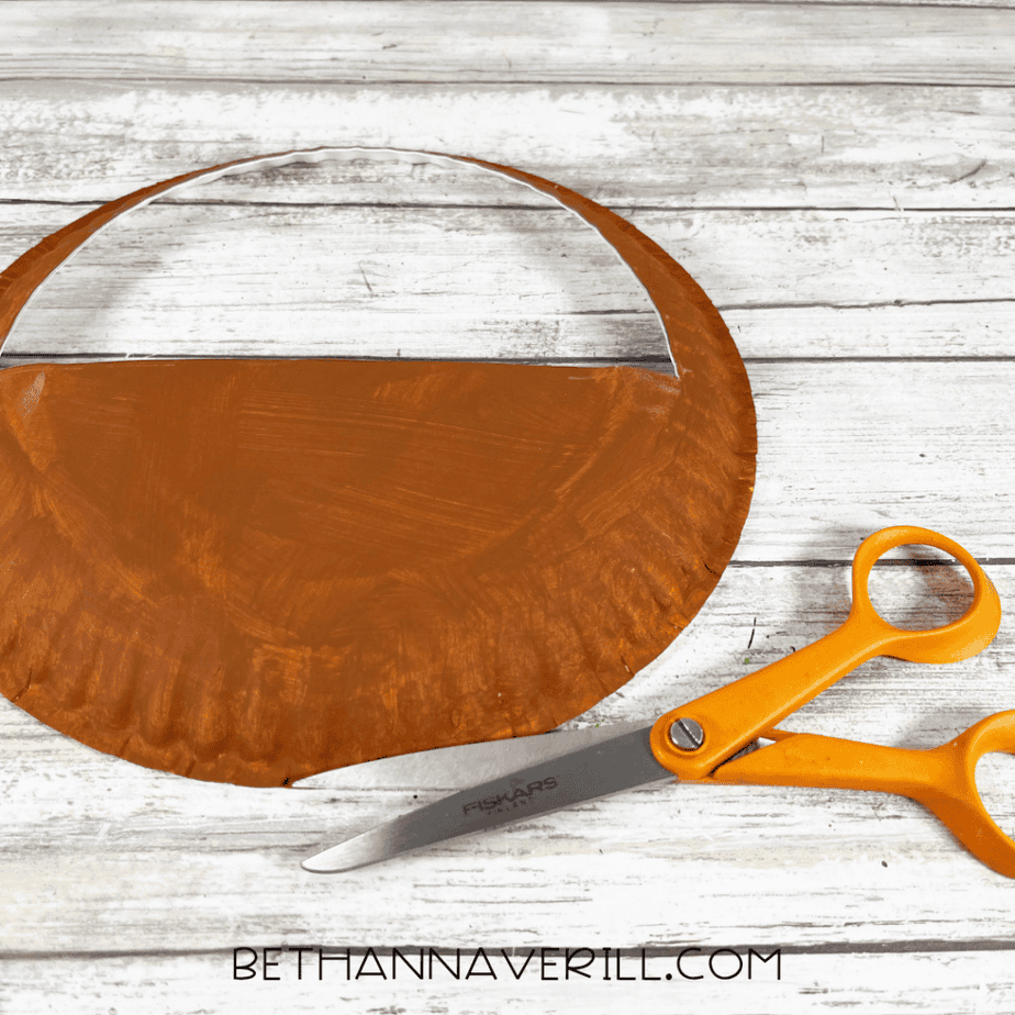 Painted paper plate cut into a basket shape with scissors on a wood surface