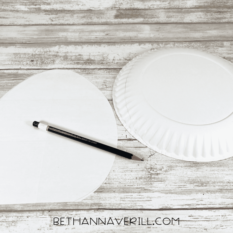 A paper plate with a pencil outline marking a rounded egg shape cut from the plate.