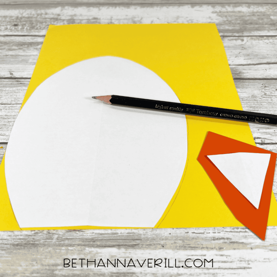 The egg-shaped plate piece placed on yellow paper with a pencil and a small orange triangle cutout nearby.